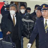 A suspect in recent shoplifting and food-tampering incidents is escorted by police at JR Shinagawa Station on Sunday. | KYODO