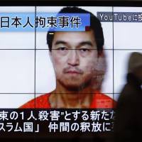 A man walks past screens displaying a television news program showing an image of Kenji Goto, one of two Japanese citizens taken captive by Islamic State militants, on a street in Tokyo on Sunday. Doubts grow over voice, image differences in Yukawa death video