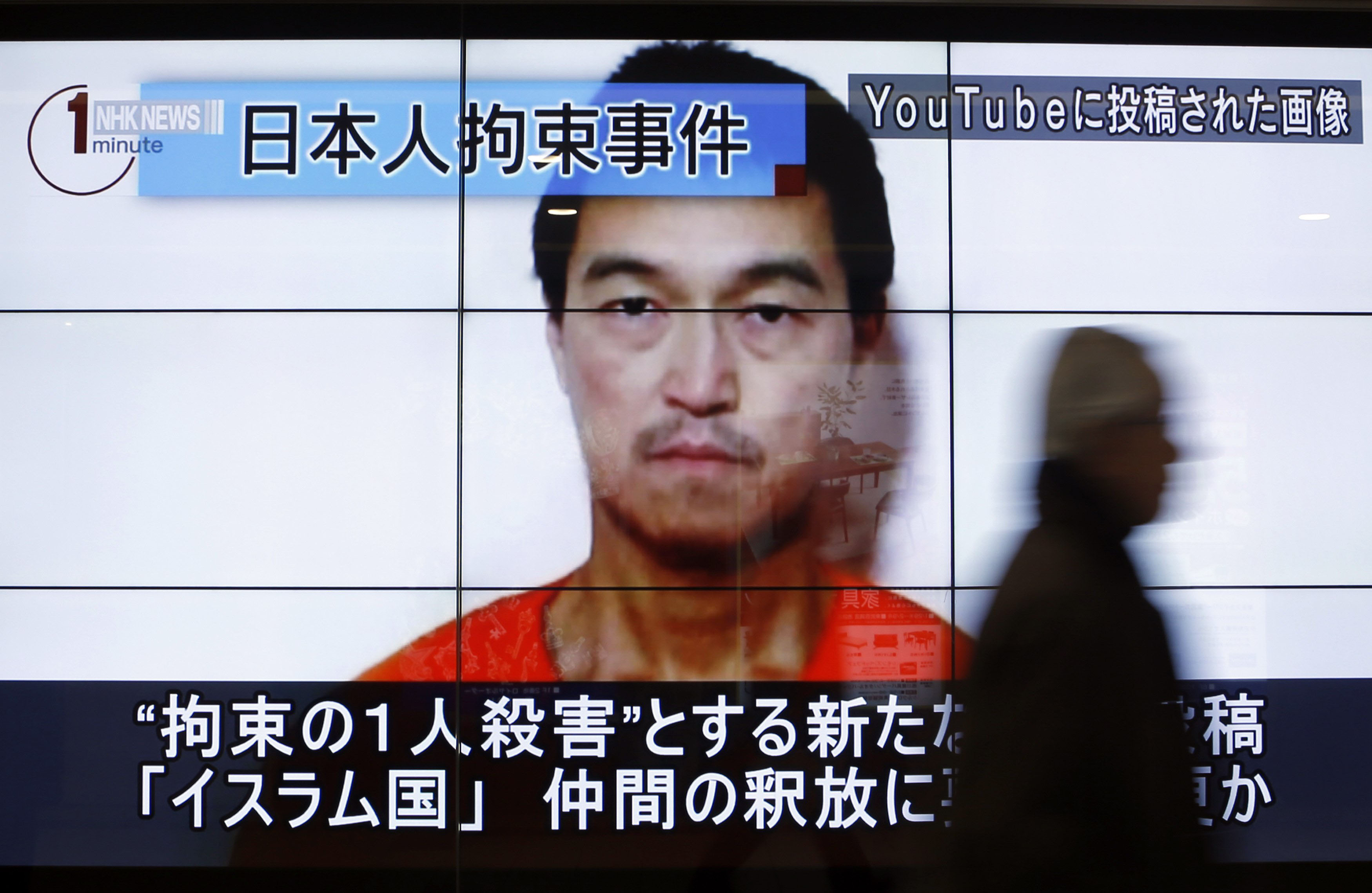 A man walks past screens displaying a television news program showing an image of Kenji Goto, one of two Japanese citizens taken captive by Islamic State militants, on a street in Tokyo on Sunday. | REUTERS