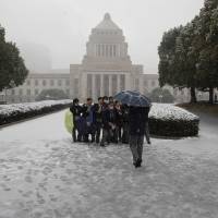 Students take pictures in front of the Diet building Friday as snow fell in Tokyo and other areas in the Kanto region. | REUTERS