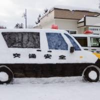 Police officer Masashi Onishi pauses for a photo on Tuesday next to a snow-car he made outside a police box in Horonobe, Hokkaido. The life-sized vehicle has set Twitter afire, with users commenting on his realistic depiction of a patrol car. | HOKKAIDO POLICE DEPARTMENT/KYODO