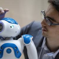 Sebastien Cagnon, behavior architect at Aldebaran Robotics SA (right), holds a demonstration with the firm\'s NAO robot at the International Robot Exhibition 2013 in Tokyo in November 2013. Mitsubishi UFJ Financial Group Inc. will trial the device in two branches in Tokyo. | BLOOMBERG