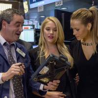 A trader shows 2015 Sports Illustrated swimsuit models Ashley Smith (center) and Hannah Ferguson a handheld device on the floor of the New York Stock Exchange on Friday. | REUTERS