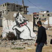 Palestinians walk past a mural of a kitten, presumably painted by the British street artist Banksy, on the remains of a house that witnesses said was destroyed by Israeli shelling last summer in the northern Gaza Strip town of Biet Hanoun, on Thursday. | REUTERS