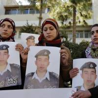 Anwar Tarawneh (center), the wife of Jordanian pilot Mu\'ath al-Kaseasbeh, holds a picture of her husband during a student-led rally calling for his release at Jordan University in Amman on Tuesday. | REUTERS