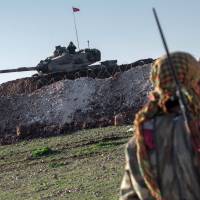 A Syrian Kurdish militia member of YPG patrols near a Turkish Army tank, as Turks work to build a new Ottoman tomb in the background in Aleppo province, Syria, on Sunday. | AP