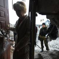 A pro-Russian fighter looks on as a woman enters her home Sunday after it was damaged by shelling the day before in the suburbs of the eastern Ukrainian city of Donetsk. | AFP
