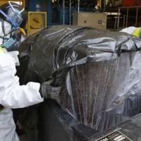 Workers wearing protective gear put compressed radioactive waste into a protective storage bag in March 2013 at a temporary storage site in Naraha, Fukushima Prefecture, inside the restricted zone near the Fukushima No. 1 nuclear power plant. | AP