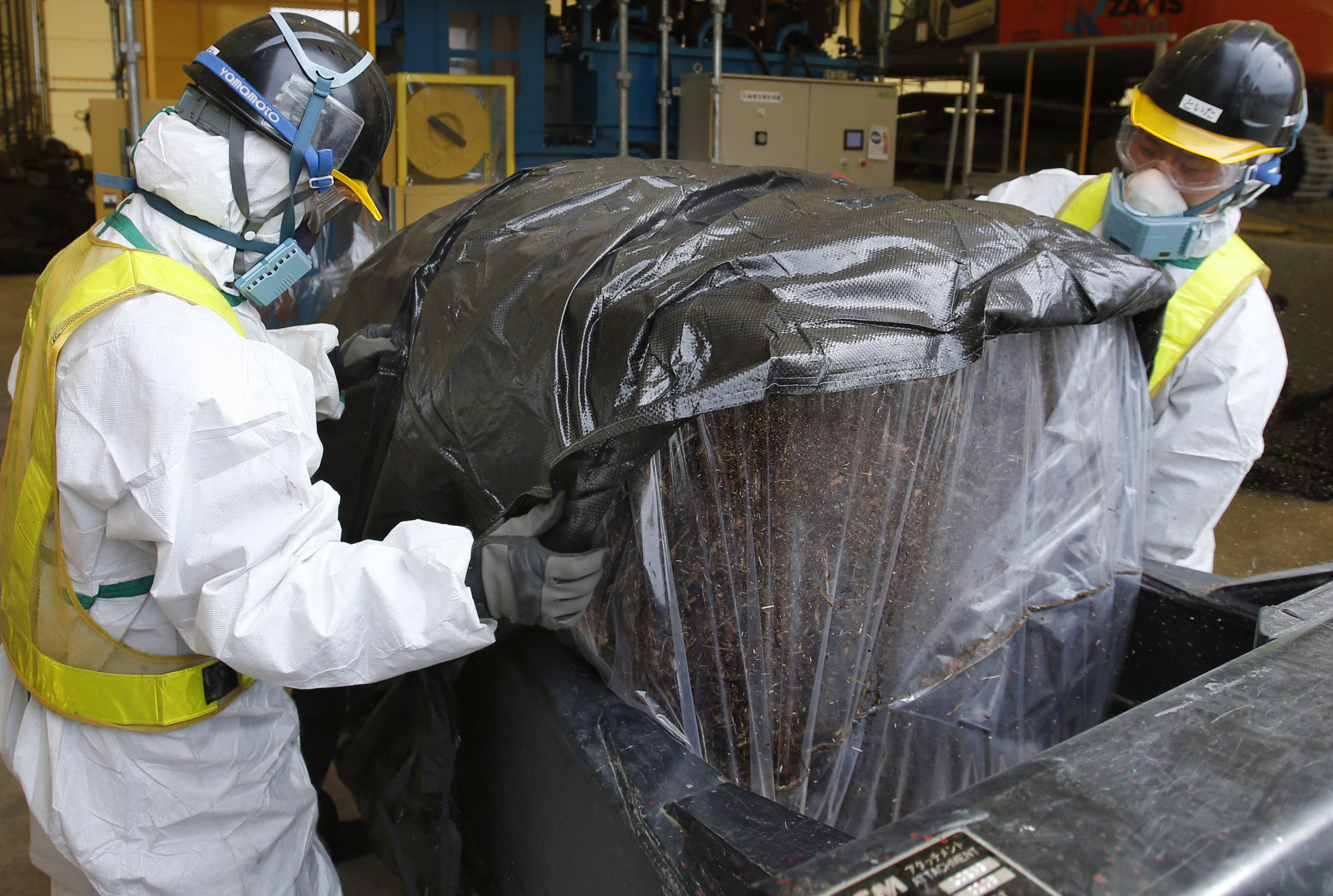 Workers wearing protective gear put compressed radioactive waste into a protective storage bag in March 2013 at a temporary storage site in Naraha, Fukushima Prefecture, inside the restricted zone near the Fukushima No. 1 nuclear power plant. | AP
