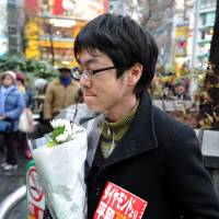A 30-year-old company worker, who asked not to be identified, holds a bouquet and a copy of Kenji Goto\'s book \"Daiyamondo Yori Heiwa ga Hoshii\" (\"We Want Peace, Not Diamonds\"), the story of a child soldier in Sierra Leone, during a mourning event for him journalist and fellow slain hostage Haruna Yukawa at Hachiko square in Tokyo\'s Shibuya district on Sunday. | YOSHIAKI MIURA
