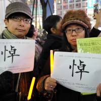 Kanako Takahashi (right), a Tokyo company employee and a friend of Kenji Goto, joined Sunday\'s event in Shibuya\'s Hachiko square with a friend. \"I\'m sad, and I\'m full of regret. What do we do without him?\" she said. The Chinese character on their placards means \"mourning\"; underneath is a quote from Goto. | YOSHIAKI MIURA