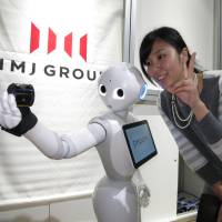 A member of Tokyo-based software team IMJ Corp. takes a photo with humanoid robot Pepper, developed by telecom company SoftBank Corp., during a application software contest for the robot held in Tokyo on Sunday. | KAZUAKI NAGATA