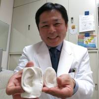 Tsuyoshi Takato, a professor of tissue engineering at the University of Tokyo School of Medicine, shows ear models. The one on the right was printed with polylactic acid, while the other was made with silicone in a mold. | KAZUAKI NAGATA