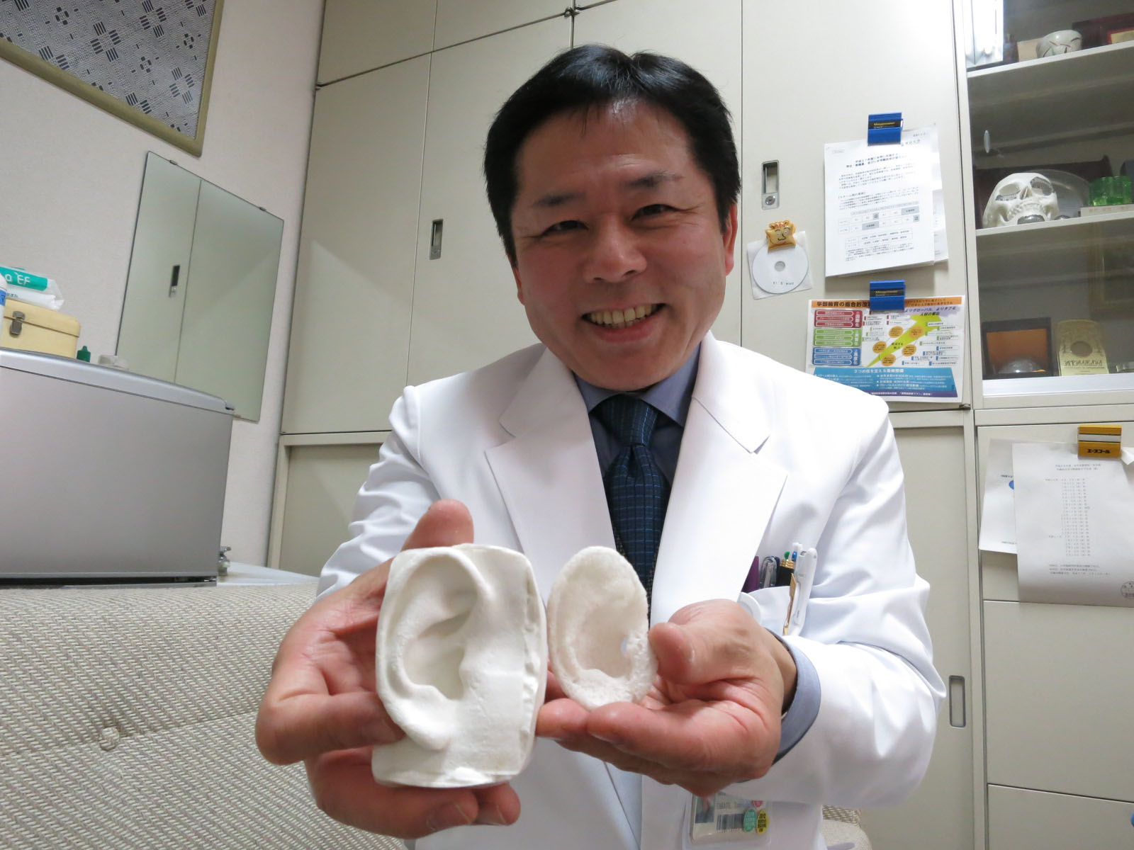 Tsuyoshi Takato, a professor of tissue engineering at the University of Tokyo School of Medicine, shows ear models. The one on the right was printed with polylactic acid, while the other was made with silicone in a mold. | KAZUAKI NAGATA