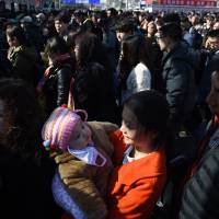 A young woman holds a baby as they wait to enter a Beijing railway station Tuesday. Hundreds of millions of Chinese are returning to their hometowns to celebrate the Lunar New Year with families in what is the world\'s largest annual migration. | AFP-JIJI