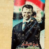A damaged picture of Syrian President Bashar Assad is seen on a wall in Idlib city, after rebel fighters took control of the area Saturday. The text on the poster reads in Arabic \"With Bashar.\" Assad said Sunday on CBS \"60 Minutes\" that the Islamic State group has expanded since the start of U.S.-led airstrikes in Syria and Iraq. | REUTERS