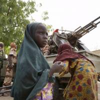 A girl stands in front of soldiers from Niger and Chad in the recently retaken town of Damasak, Nigeria, on Friday. | REUTERS