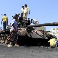 People gather near a tank gutted during clashes on a street in Yemen\'s southern port city of Aden on Sunday. Yemeni fighters loyal to the Saudi-backed President Abd-Rabbu Mansour Hadi clashed with Iranian-allied Houthi fighters on Sunday in downtown Aden, the absent leader\'s last major foothold in the country. | REUTERS
