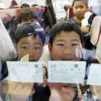 Children riding a Kagayaki bullet train show off their tickets Saturday morning at JR Nagano Station after the Hokuriku Shinkansen Line opened for business. | KYODO