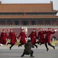 Chinese hostesses serving delegates from the National People\'s Congress, jump as they pose for photos in Tiananmen Square in Beijing on Thursday. | AP