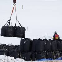 Bags of radiation-tainted soil are moved by a machine in Iitate, Fukushima Prefecture, in March 2014. The government plans to ratchet up its publicity campaign on the need to build permanent disposal sites for nuclear waste after being criticized for promoting nuclear power without already having such storage facilities in place. | BLOOMBERG