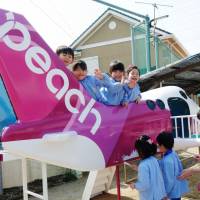 Nursery school children paint airplane-shaped playground equipment with the colors and logo of Peach Aviation on Friday in the city of Izumisano, Osaka Prefecture, which hosts Kansai International Airport. The budget carrier held the event to teach the pupils about the jobs of pilots and flight attendants and to whet their appetite for the airline industry. | KYODO