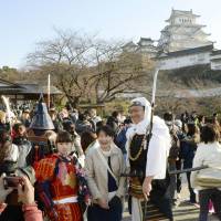 People pose in feudal period costumes Friday at Himeji Castle in Himeji, Hyogo Prefecture, as the castle\'s renovated donjon, seen behind, was opened to the public after more than five years of repair work. | KYODO