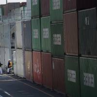 Port workers converse at a container terminal in Tokyo. Exports exceeded imports in March for the first time in almost three years. | AP