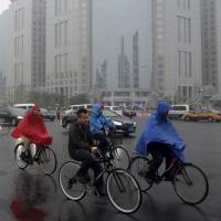Residents ride their bicycles next to vehicles traveling along Chang\'an Avenue in the rain on a hazy day in central Beijing on Tuesday. Beijing has introduced measures to limit the number of motorists on heavily polluted days, the latest move by authorities in the Chinese capital to battle the choking smog that has blanketed the city in recent years. | REUTERS