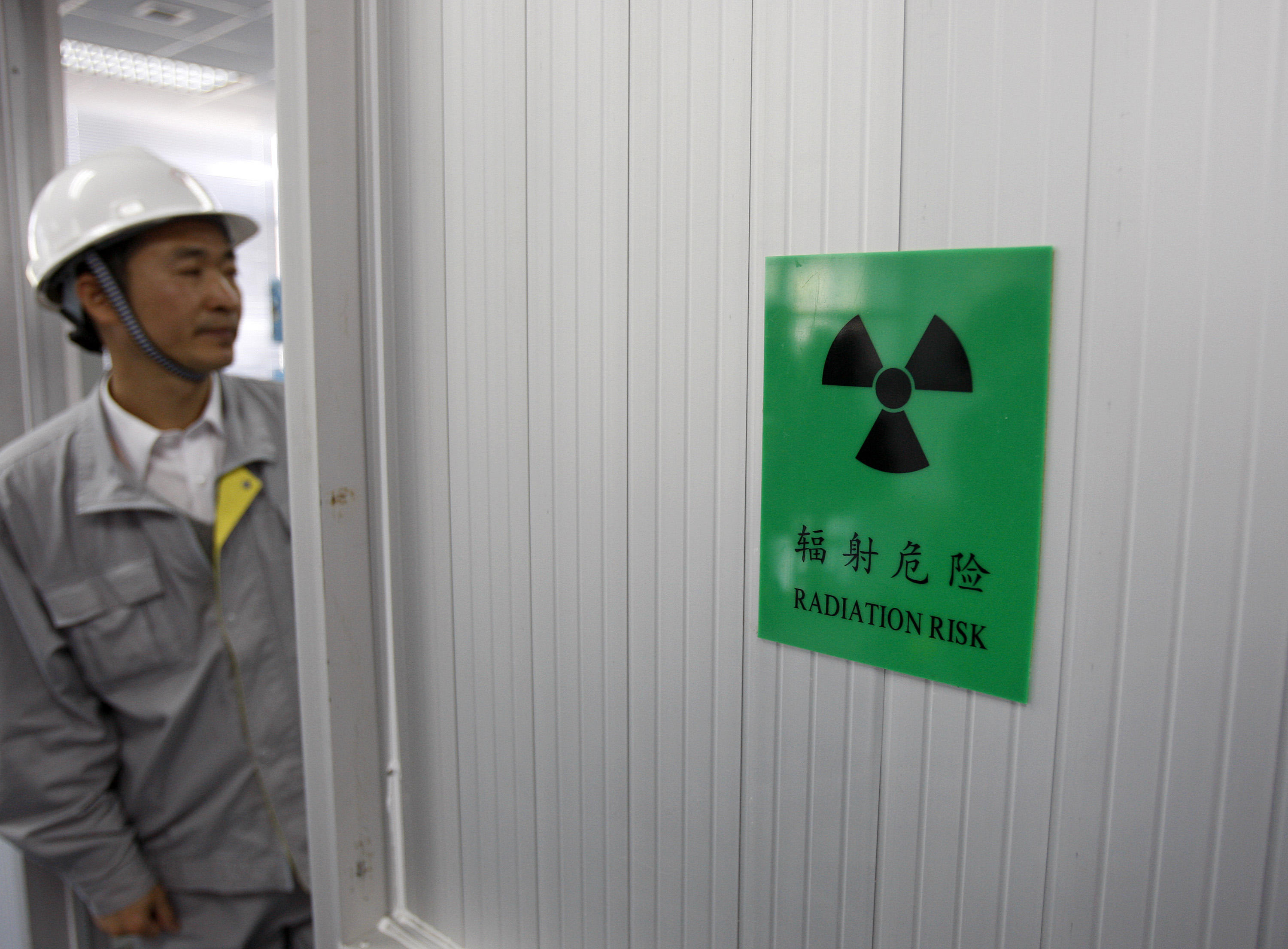 A trainer for the Daya Bay Nuclear Power Operations and Management Company stands near a radiation sign in Daya Bay, near Shenzhen, China, in December 2009. | BLOOMBERG