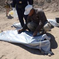 A member from the Iraqi forensic team writes on the body bag of remains belonging to Shiite soldiers from Camp Speicher who were slain by Islamic State militants and put in a mass grave in Tikrit. | REUTERS