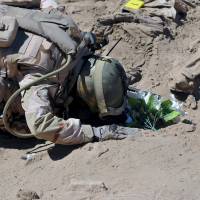 A soldier prays at a mass grave for Shiite soldiers from Camp Speicher who were murdered last summer by Islamic State militants in Tikrit. | REUTERS