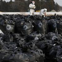 Workers work on bags containing soil, leaves and other debris from the decontamination operation in Tomioka, Fukushima Prefecture, near Tepco\'s Fukushima No. 2 nuclear power plant, on Feb. 24. | REUTERS
