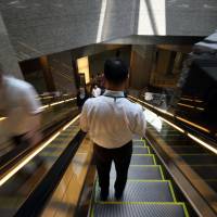 A man rides on an escalator in Tokyo last July. Prime Minister Shinzo Abe\'s administration has submitted a bill to the Diet that would allow companies to exempt skilled, well-paid workers from work-hour regulations, a move that proponents say would help boost productivity. | BLOOMBERG