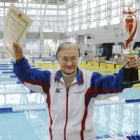 Swimmer Mieko Nagaoka, 100, smiles as she holds up a diploma and trophy after setting a world record in a 1,500-meter event held in Matsuyama, Ehime Prefecture, on Saturday. | KYODO
