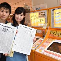 Taku Mitani and his wife, Momoko, hold copies of old front pages of The Japan Times, at Hakuhinkan Toy Park in Tokyo\'s Ginza district. The machine beside them produces front-page copies of any issue of the newspaper published between 1897 and 2014. For added nostalgia, it also offers the TV listings, radio page or back page of the issue. | SATOKO KAWASAKI