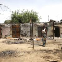 A woman stands Sunday in front of a gutted building in Michika, Nigeria, after the military recaptured it from Boko Haram, in Adamawa state. | REUTERS