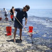 William McConnaughey, 56, (right) who drove from San Diego to volunteer, carries buckets of oil from an oil slick in bare feet along the coast of Refugio State Beach in Goleta, California, Wednesday. A pipeline ruptured along the scenic California coastline on Tuesday, spilling some 21,000 gallons (79,000 liters) of oil into the ocean and on beaches before it could be secured, a U.S. Coast Guard spokeswoman said. | REUTERS