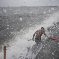 Storm-whipped waves strike the shore near Manila as a man retrieves rubber slippers on Sunday. About 2,500 residents in two provinces huddled in shelters following evacuation warnings. | AP