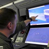 A U.S. Navy crewman aboard a P-8A Poseidon surveillance aircraft views a computer screen purportedly showing Chinese construction on the reclaimed land of Fiery Cross Reef in the disputed Spratly Islands in the South China Sea, in this still image from video distributed May 21. | U.S. NAVY / REUTERS