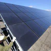Hideki Yoshida, an electrical engineer at Japan Asia Group Ltd., inspects solar panels at the Kushiro Hoshigaura SolarWay solar photovoltaic power plant run by unit Kokusai Kogyo Holdings Co. in Kushiro, Hokkaido, in May 2013. | BLOOMBERG