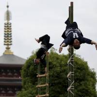 Men wearing costumes worn by traditional firefighters perform acrobatic stunts atop bamboo ladders following a memorial service for firefighters at Sensoji Temple in Tokyo\'s Asakusa area on Monday. Hundreds of firefighters wearing traditional garb gathered for the service to remember their comrades killed in the line of duty over the last 300 years. The temple\'s five-story pagoda can be seen behind the firefighters. | REUTERS