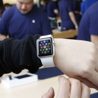 A customer tries on an Apple Watch at an Apple Store in Hong Kong  in April. Two months after Apple began taking online orders for its newest product, the company on Thursday said it will begin selling some models in its retail stores in two weeks. Apple also says it\'s cutting through a backlog of online orders, with most watches ordered by the end of May shipping within two weeks. | AP