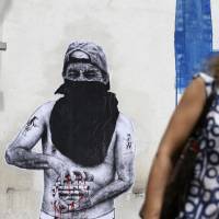 A pedestrian in Athens on June 22 walks past graffiti depicting a protester squeezing a euro. On Monday the European Union is to briefly put aside worries about Greece to broaden its relations with China at a summit in Brussels. | AP