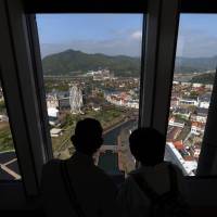 A couple look out of an observation deck at the Dutch-themed Huis Ten Bosch theme park in Sasebo, Nagasaki Prefecture. Hideo Sawada, the chairman of travel agency H.I.S. Co. and also the president of the park operator, says he is turning to robots to help revive the bubble-era dud. | BLOOMBERG