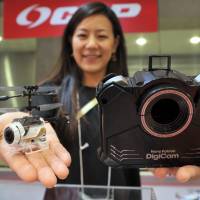 A CCP Co. employee shows off the Nano Falcon DigiCam, a remote-controlled copter that can shoot photos or videos from the air, at International Tokyo Toy Show 2015 at Tokyo Big Sight in Koto Ward on Thursday. The 20-gram drone can also be folded up and snapped into the open cavity in the control unit to form a hand-held digital camera. | YOSHIAKI MIURA
