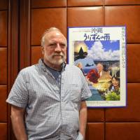 Reflecting on the legacy of war: American filmmaker John Junkerman poses in front of a promotional poster for his latest film, \"Okinawa: Urizun no Ame,\" at the Japan National Press Club in Tokyo. | MELYNIE YONEDA