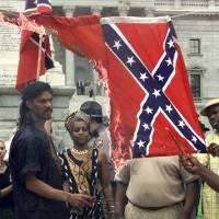 In this May 10, 2000, file photo, Kevin Gray of the Harriet Tubman Freedom House watches as a Confederate flag burns during a demonstration in Columbia, South Carolina, to protest the Confederate flag flying atop the dome of the South Carolina Statehouse. On the left side was a Nazi flag which burned first. For many black Americans, Confederate flag debate merely a distraction