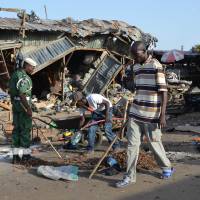 A man walks past a the scene of a bombing after at least 20 people were killed when a young female suicide bomber detonated her explosives at a bus station in Maiduguri, northeast Nigeria, on Monday in an attack likely to be blamed on Boko Haram. The blast happened near a fish market in the Baga Road area of the city, which has been repeatedly targeted in recent weeks by shelling, bombs and suicide attacks. | AFP-JIJI