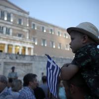 A child holds a mini Greek national flag during an anti-austerity demonstration in support of the Greek government in Syntagma Square in Athens on Monday. | BLOOMBERG